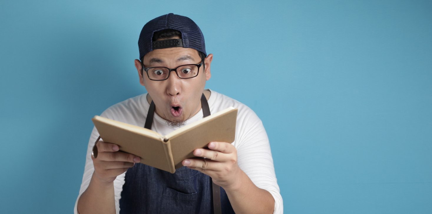 Portrait of Asian male chef reading book of recipes, finding secret recipe