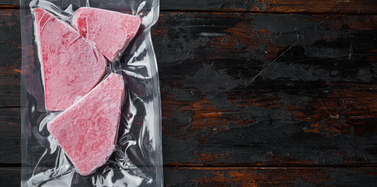 Frozen Tuna fish steak in a vacuum plastic package, on old dark wooden table background, top view flat lay , with copyspace and space for text